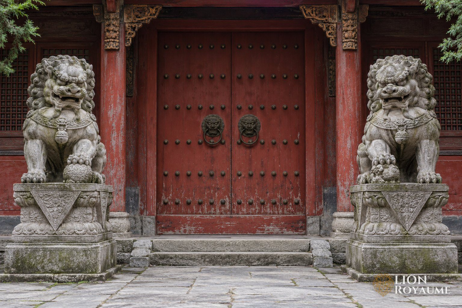 Paire de lions gardiens en pierre de part et d'autre d'une porte de temple rouge
